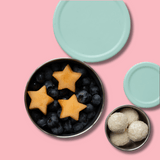 stainless steel containers with star-shaped fruit and blueberries on a pink background with mint silicone lids