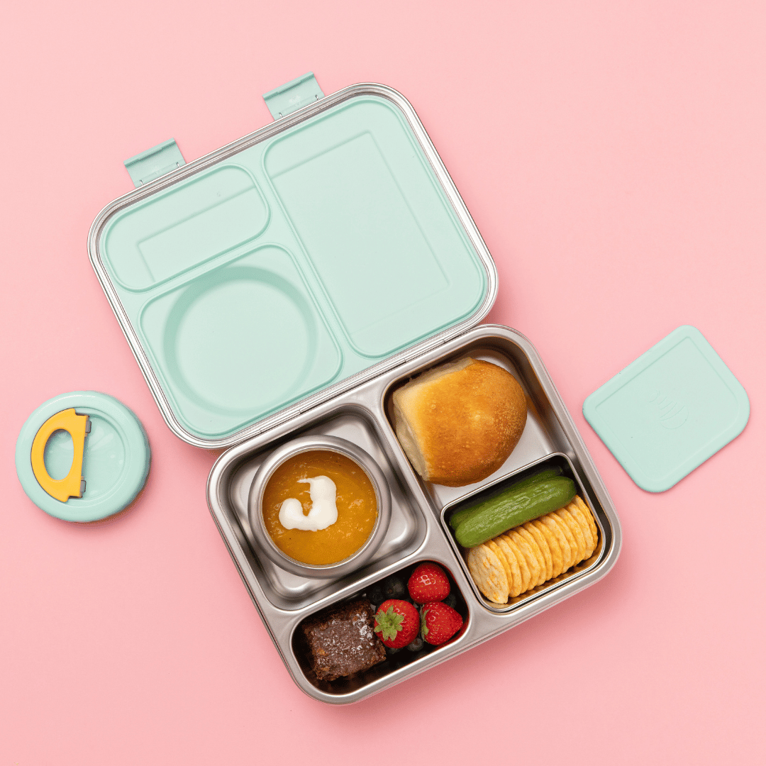 Hot n Cold stainless steel hero lunch box box in mint includes an insulated food jar that sits inside with 2 other compartments containing a sandwich, fruit, and other snacks on a pink background