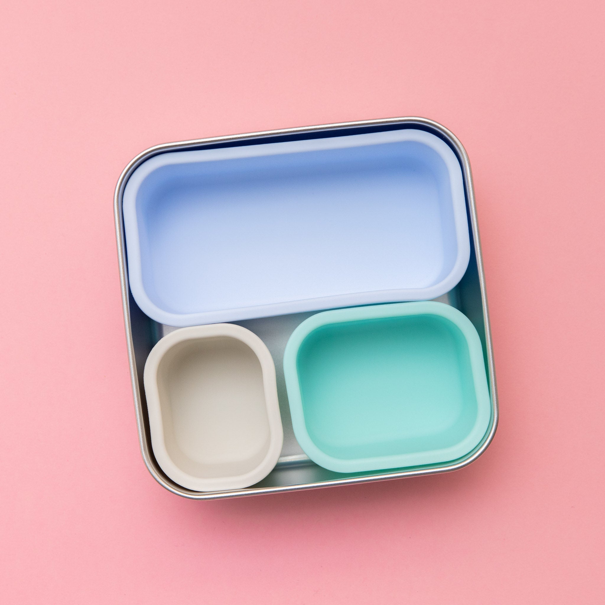 stainless steel square container or sandwich box with blue lid on a pink background empty  showing 3 coloured silicone cups inside