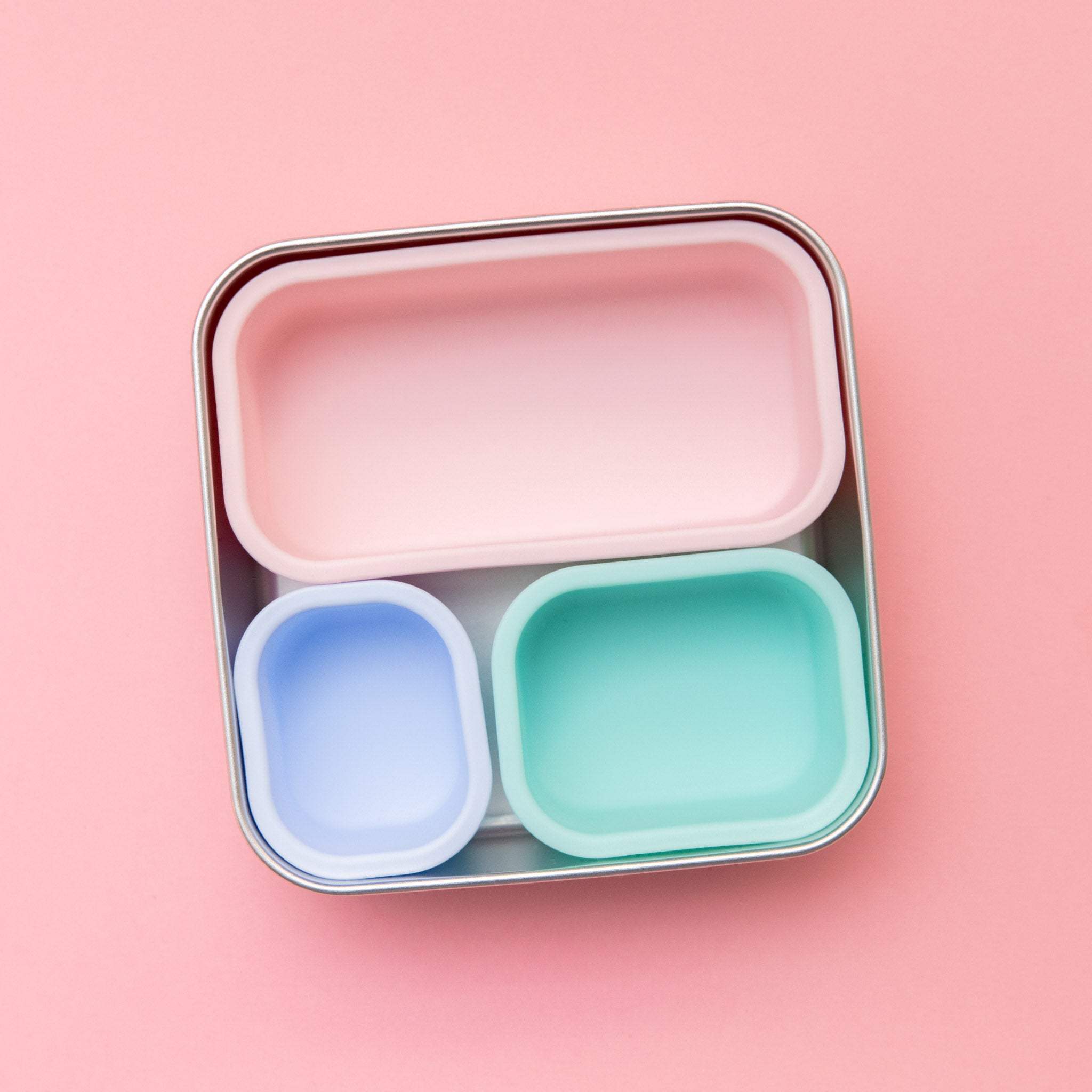 stainless steel square container or sandwich box with pink lid on a pink background containing 3 silicone cups  