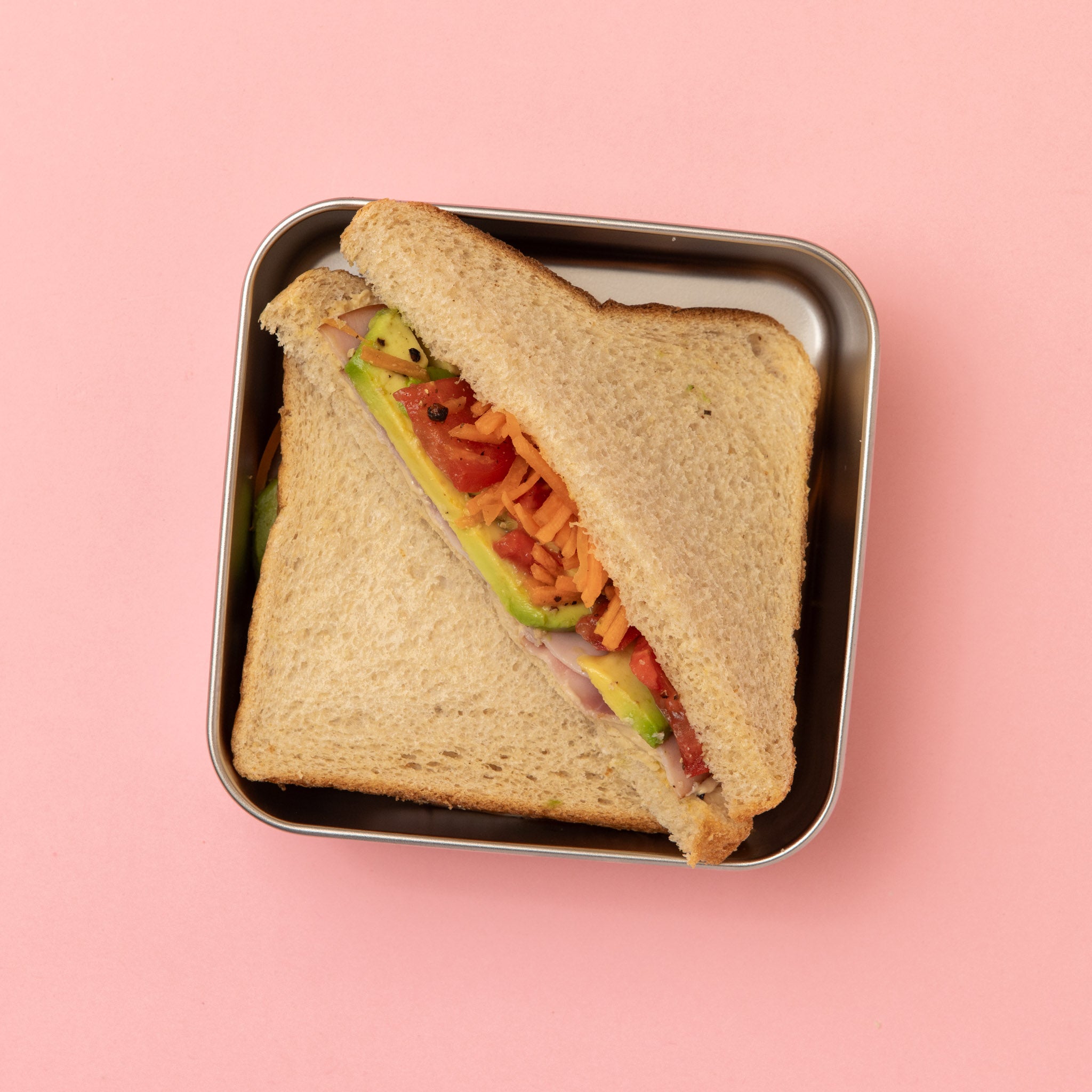 stainless steel square container or sandwich box with pink lid on a pink with a full sized sandwich 