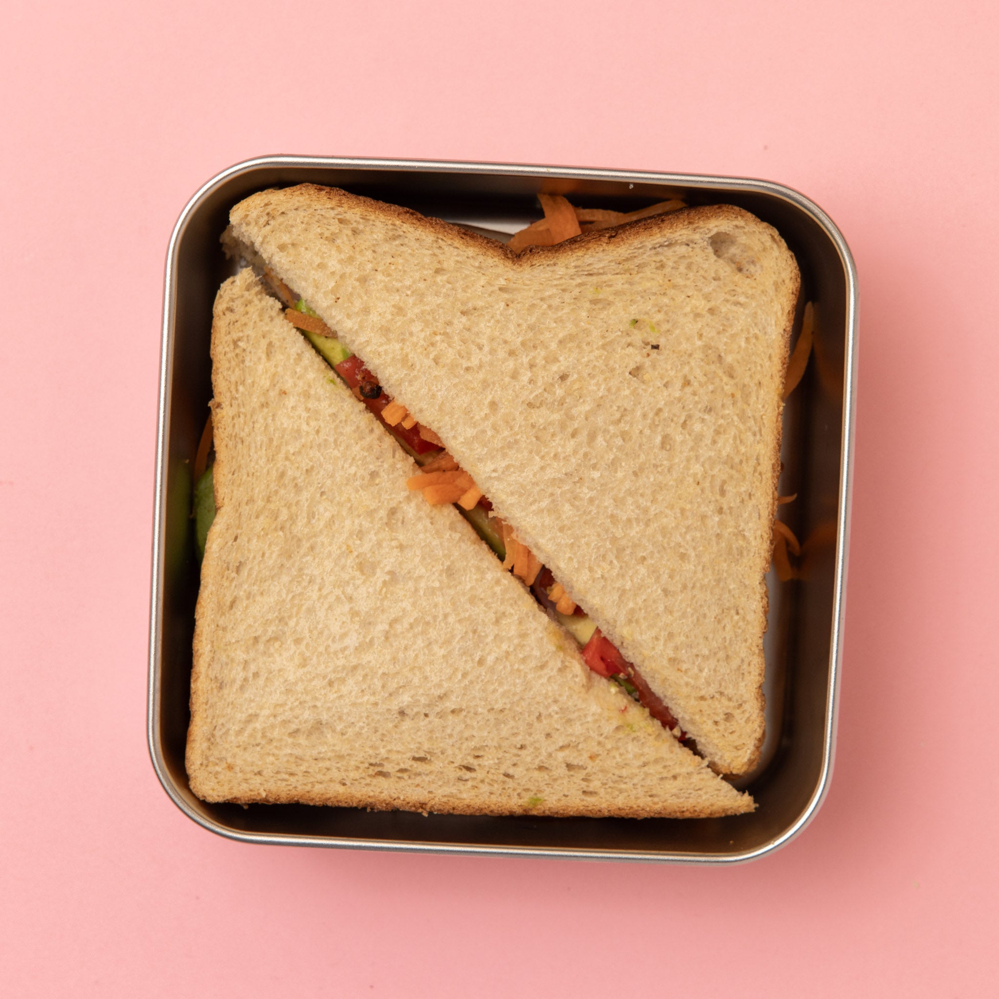 stainless steel square container or sandwich box with blue lid on a pink background with a full sized sandwich 