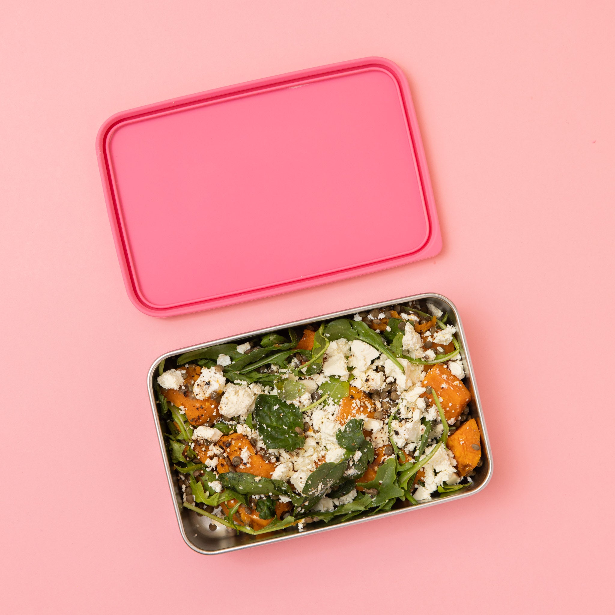 large stainless steel salad container or lunch box with dark pink  silicone lid on pink background with salad  