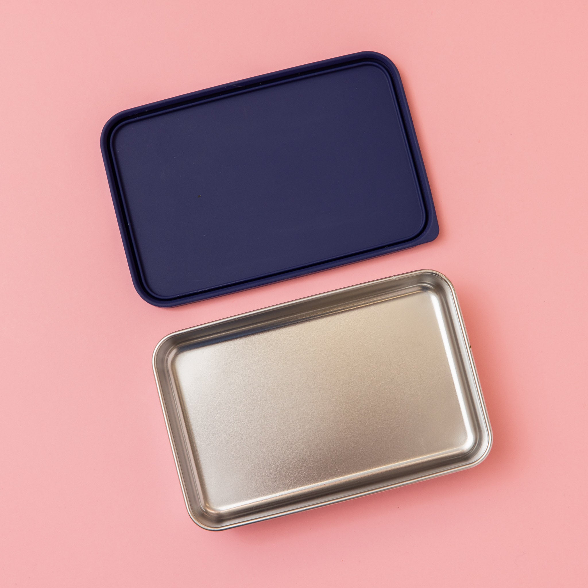 large stainless steel salad container or lunch box with navy silicone lid on pink background empty 