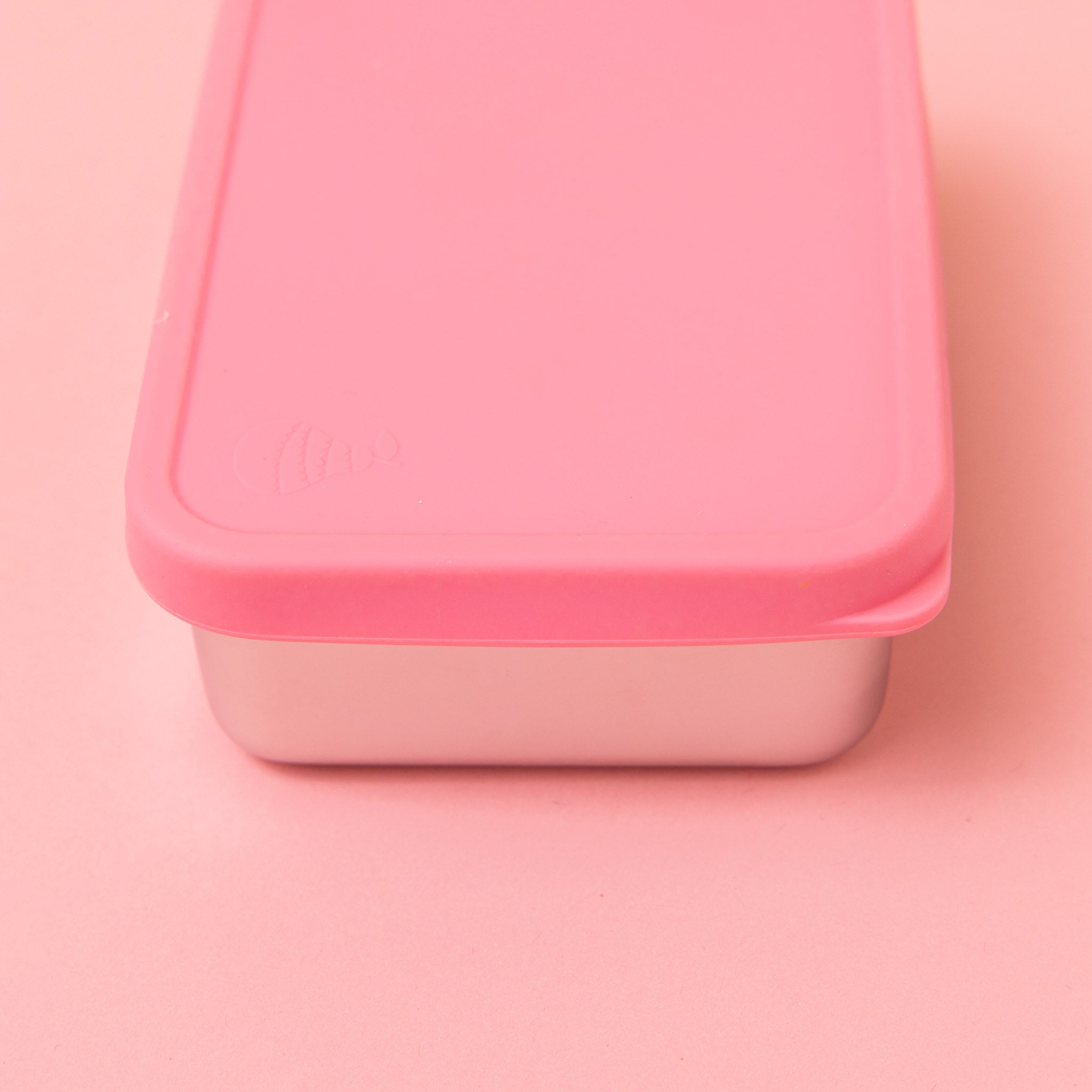 stainless steel snack container with pink silicone lid on a pink background with lid on showing pear logo on lid and tab to pull open 