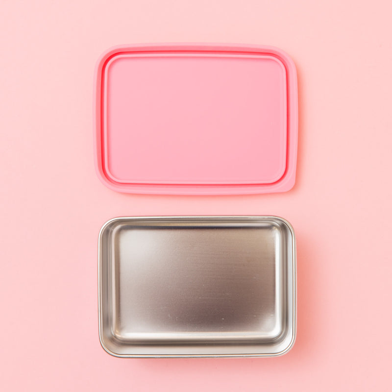 stainless steel snack container with pink silicone lid on a pink background empty
