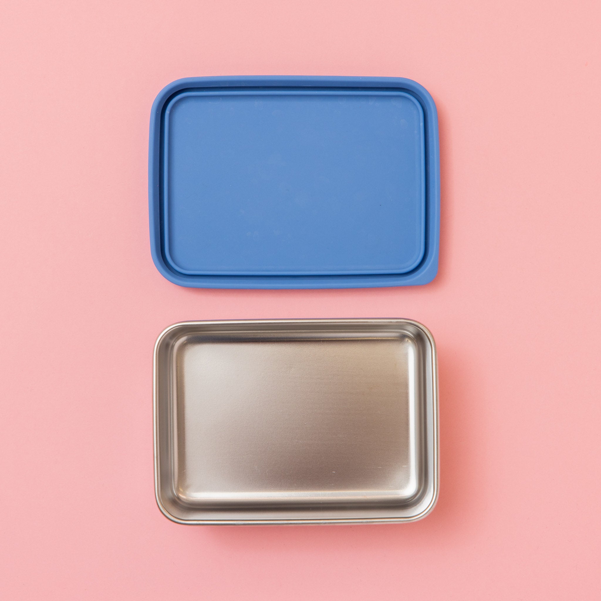 rectangular stainless steel snack container empty and blue lid on a pink background