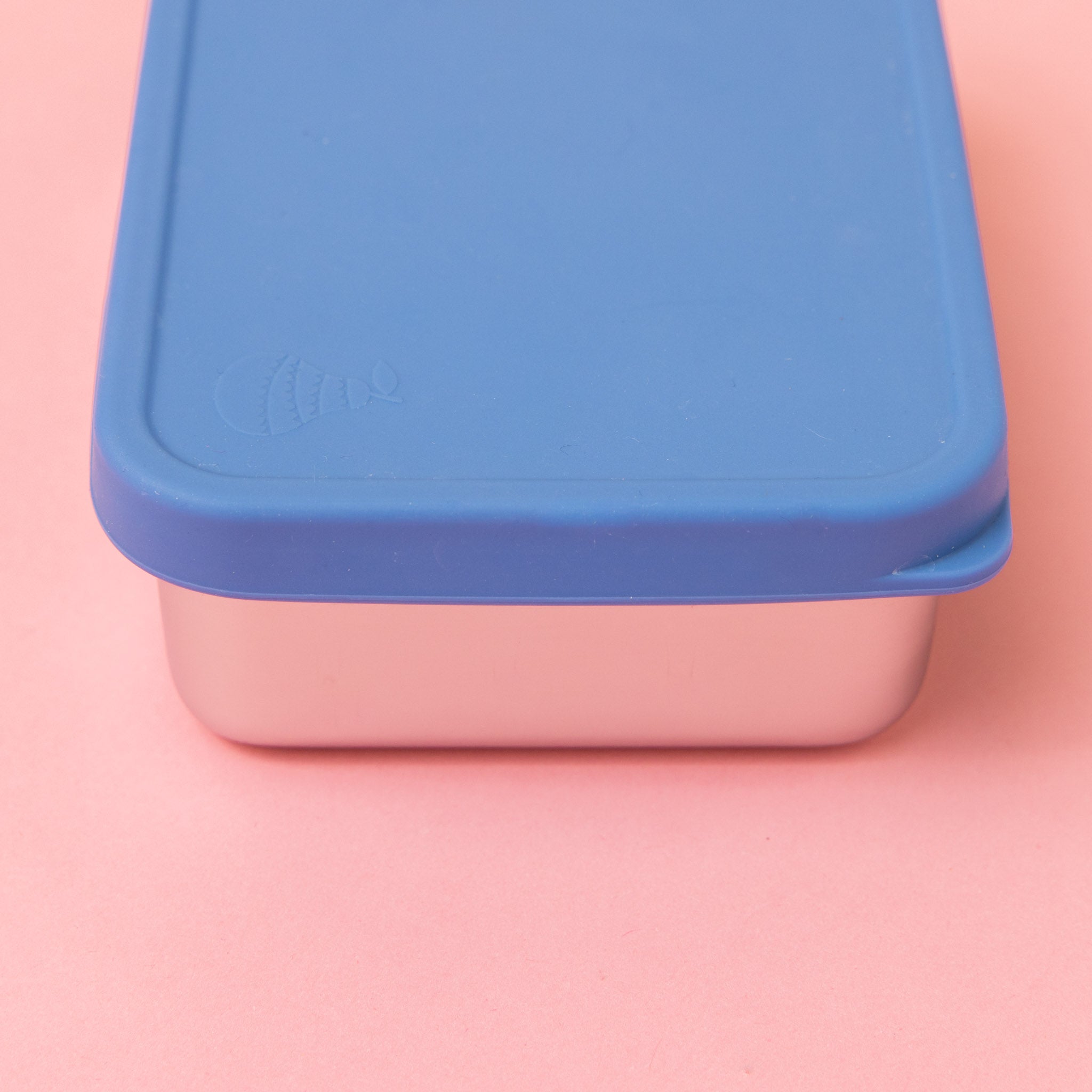 rectangular stainless steel container with silicone blue lid on a pink background