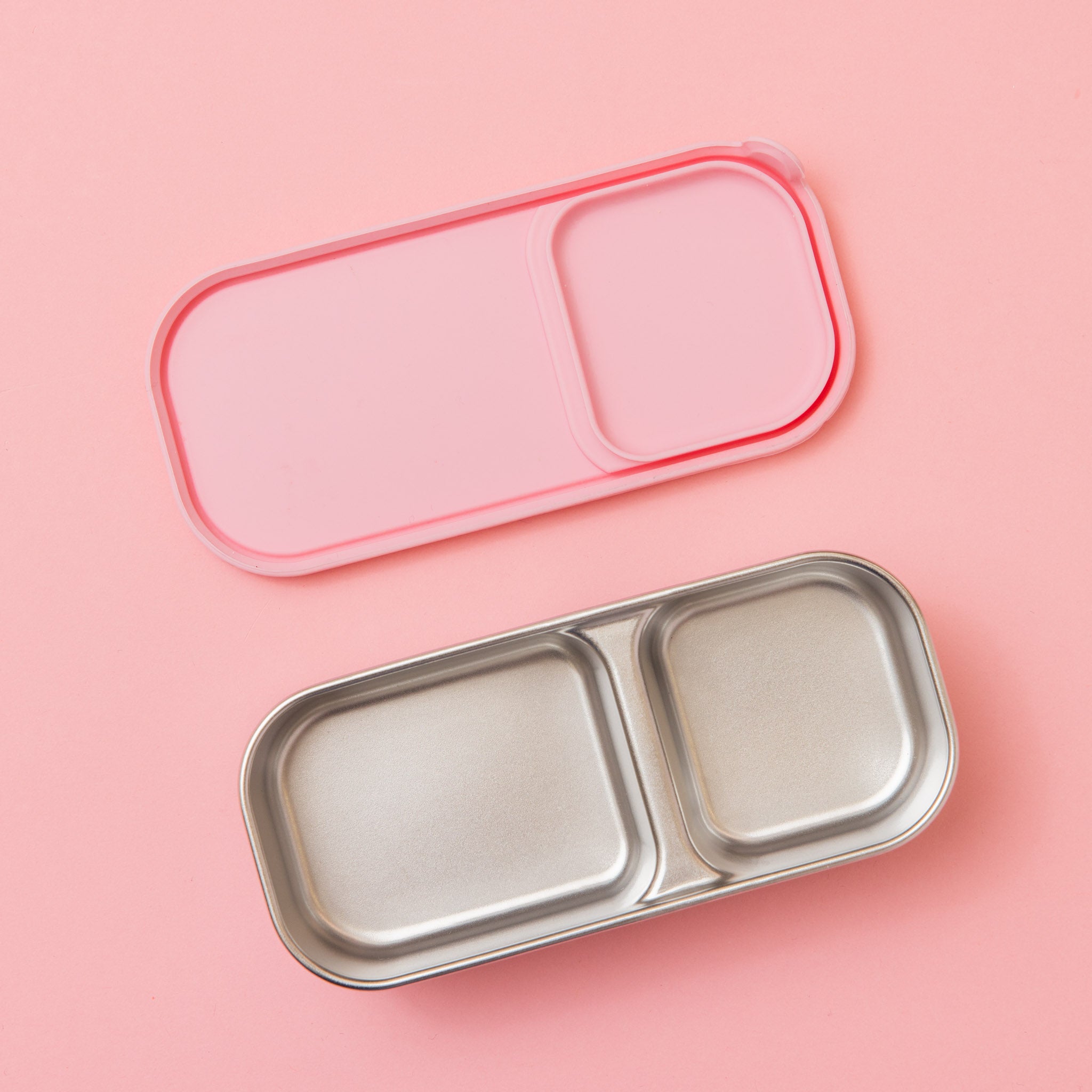 two compartment stainless steel snack container with light pink silicone lid shown from underside empty 